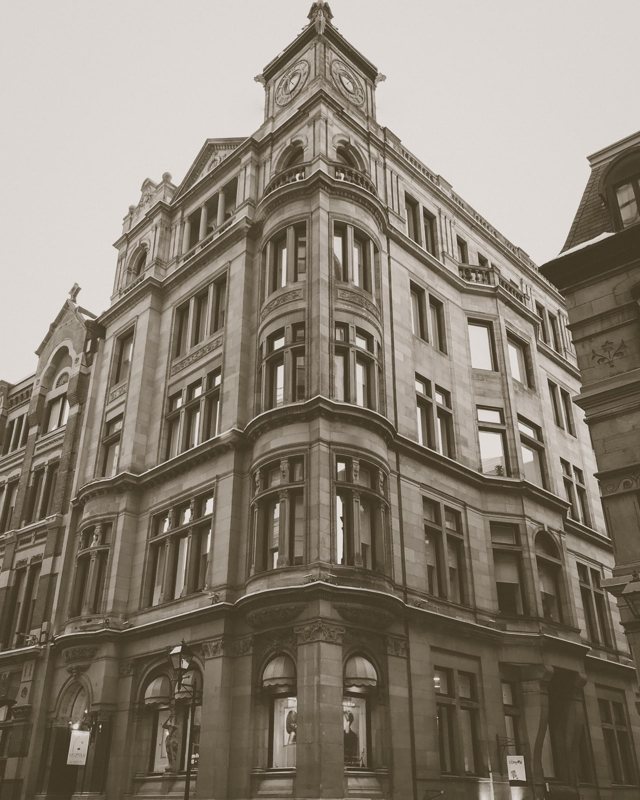 A stone corner building with bay windows and a clock tower, in muted sepia tones
