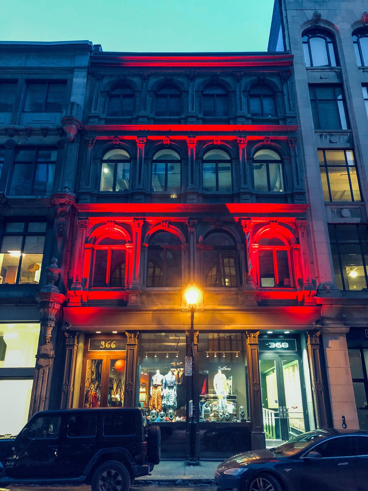 An ornate stone façade washed in red light above lit shop windows and a glowing street lamp