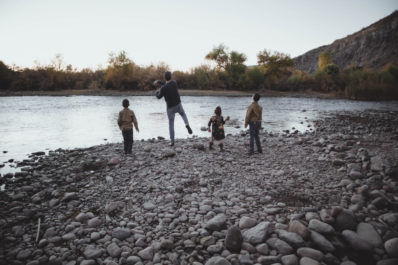 A family seen from behind, throwing stones into the Salt River from a rocky shore