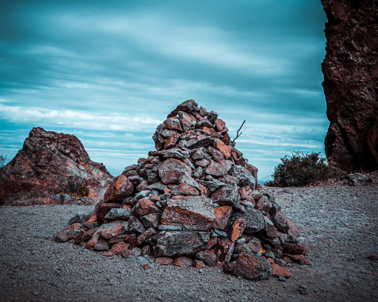 A tall cone of stacked red and grey stones on a gravel clearing between rock outcrops