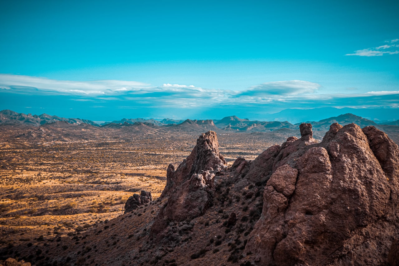 Rugged red rock crags on a ridge overlooking a golden desert plain and distant ranges