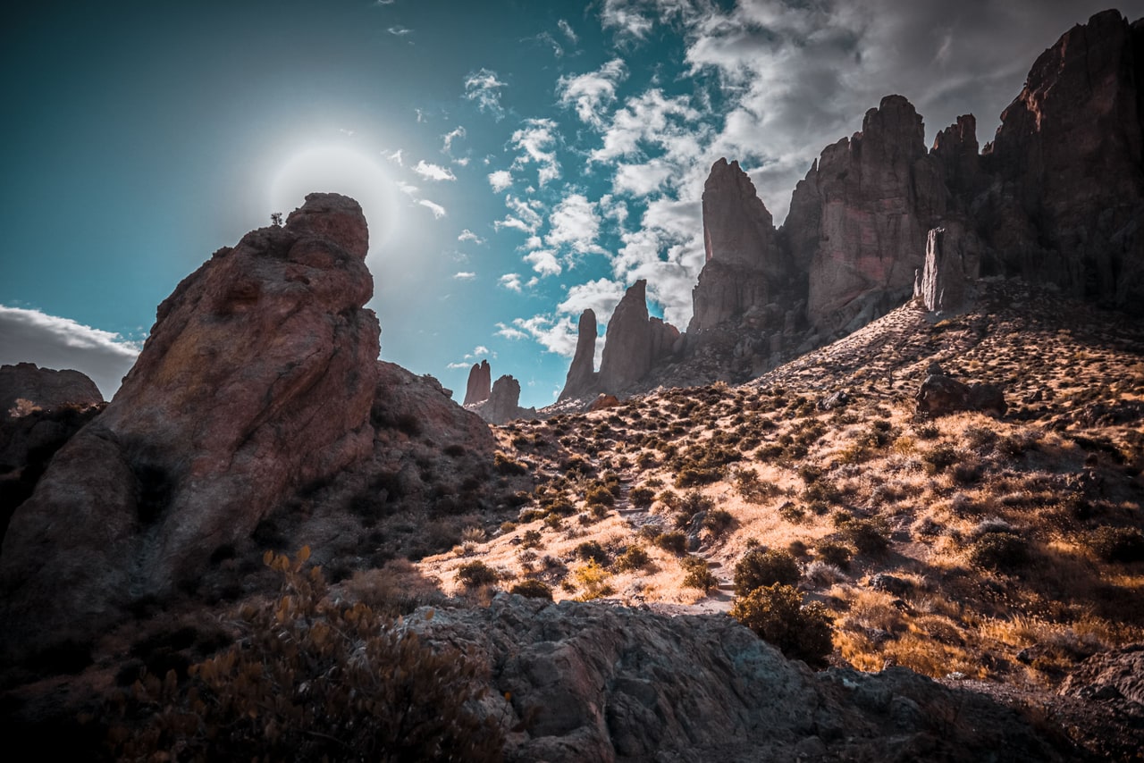 The sun haloed beside the top of a rock outcrop, with spires beyond