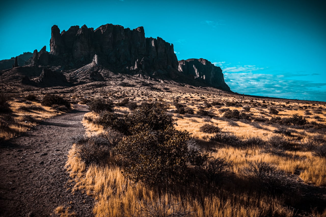 A gravel trail curving through dry golden grass toward a dark wall of cliffs