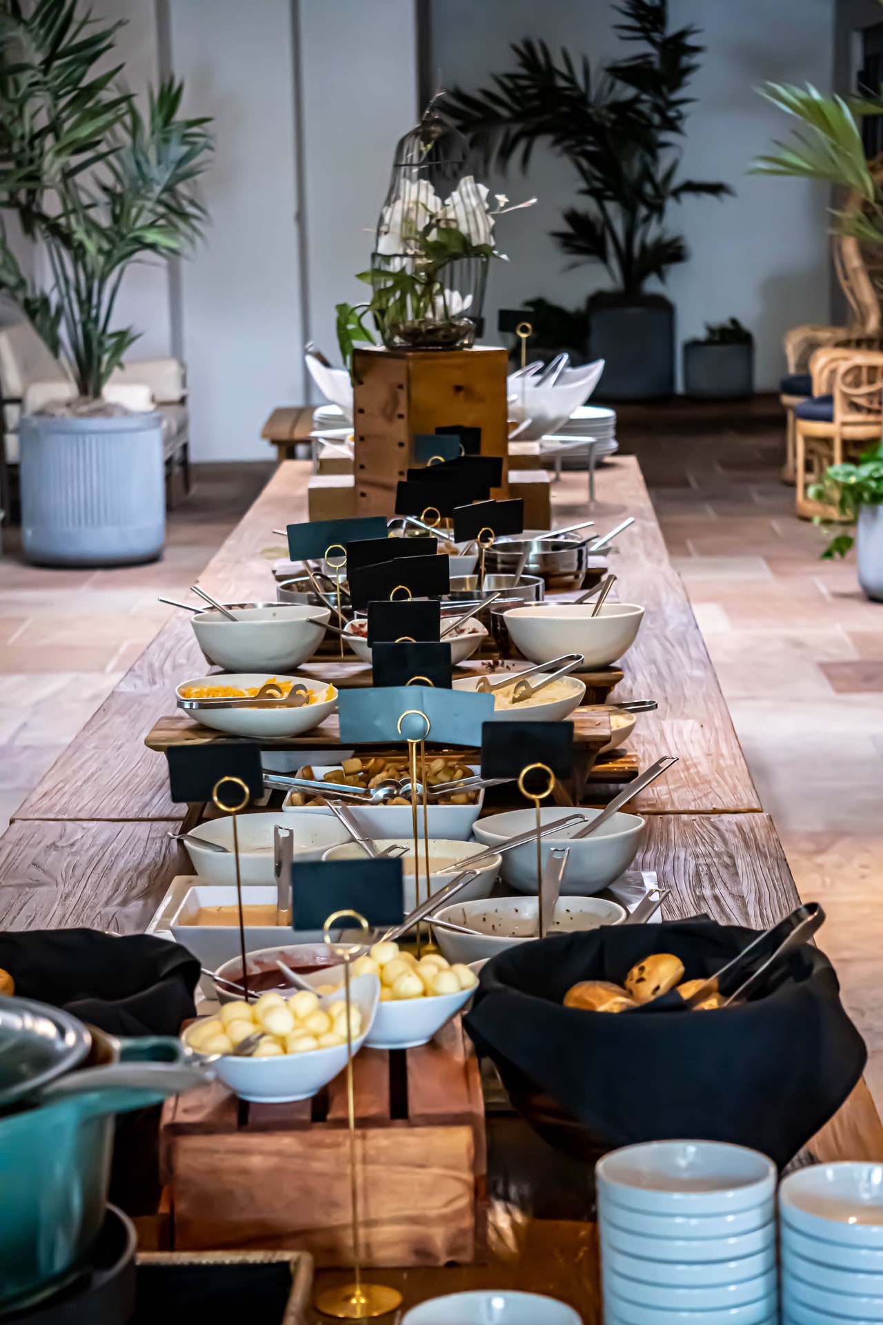 A long wooden buffet table set with bowls, bread baskets and small black label cards