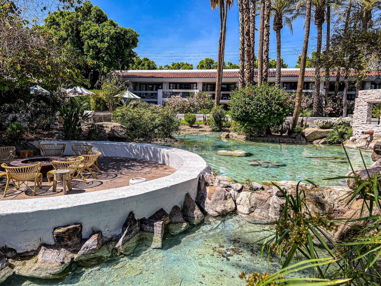 A clear turquoise lagoon pool edged with boulders beside a curved white wall enclosing rattan chairs