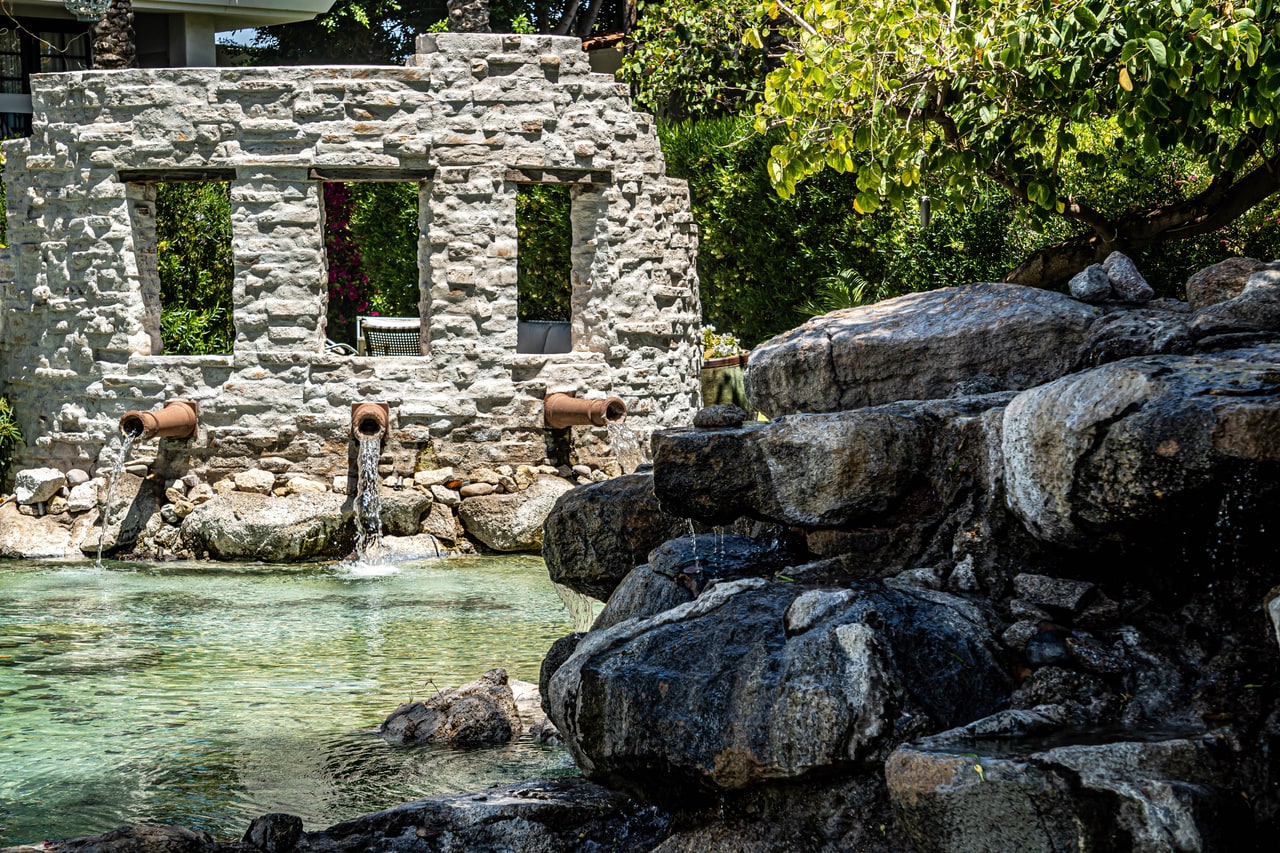 A whitewashed stone ruin with three window openings, its terracotta spouts pouring into a clear lagoon