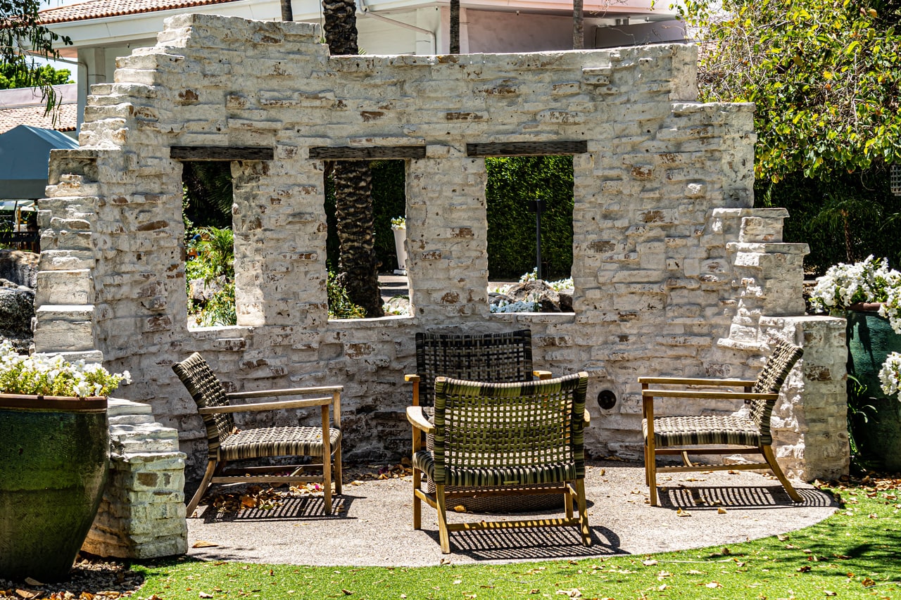 Woven lounge chairs in a circle before a whitewashed stone wall with three window openings